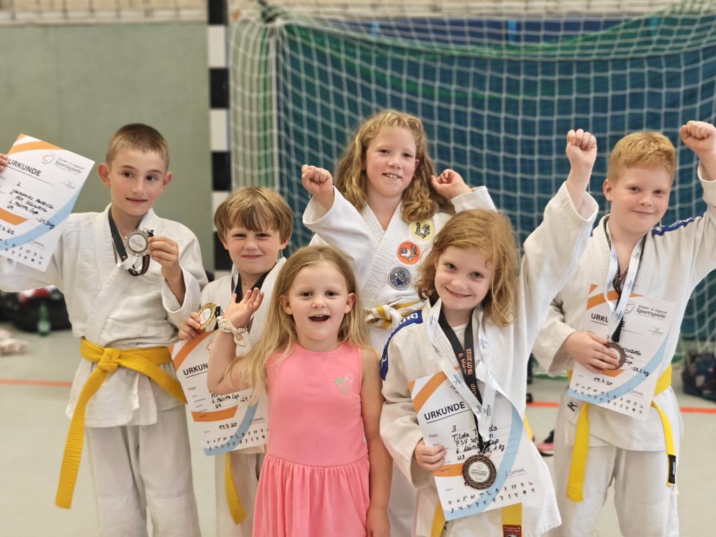 Judo-Kinder des PSV Schwerin mit Medaillen und Urkunden nach einem Wettkampf, lachend und jubelnd in der Halle.